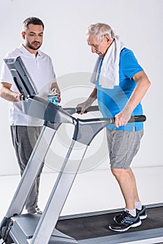 rehabilitation therapist assisting senior man with towel exercising on treadmill