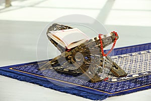 Rehal with open Quran and Misbaha on Muslim prayer rug indoors