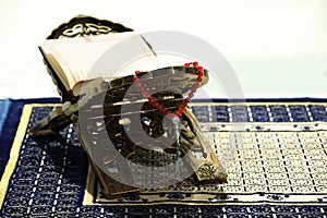 Rehal with open Quran and Misbaha on Muslim prayer rug indoors