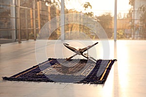 Rehal with open Quran and Muslim prayer beads on rug