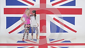 Rehearsal of two charming women in t-shirts dancing on background of UK flag.