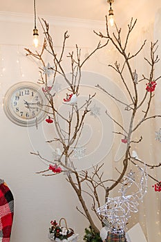 Reindeer garland, dry tree with red berries, snowflakes, clock. Happy New Year inscription on wall. Living room corner decorated