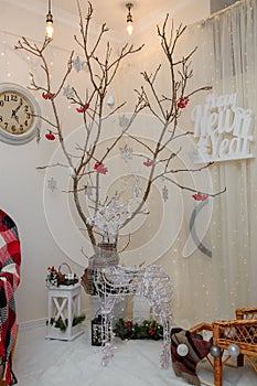 Reindeer garland, dry tree with red berries, snowflakes, clock. Happy New Year inscription on wall. Living room corner decorated