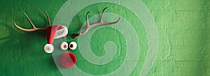 Reindeer with red nose and Santa hat on vibrant green wall background with copy space.