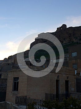 a reinforced concrete structure in a traditional city texture and the historical mardin castle in the background