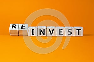 Reinvest symbol. Inverted wooden cubes with words `invest - reinvest`. Beautiful orange background. Business and reinvest concep