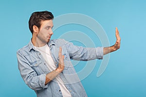 Rejection, denial concept. Side view of man in worker denim shirt doing stop sign with outstretched hands