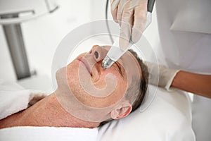 Rejuvenating facial treatment. Mature man getting lifting therapy massage in a beauty SPA salon. Exfoliation, stimulation and