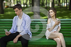 Relationship problem. Bored millennial couple using phones on dull date in park