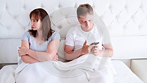 Relationship problems concept - a middle-aged couple lying in bed in the morning a man holding a smartphone. Middle age couple in
