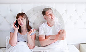 Relationship problems concept - a middle-aged couple lying in bed in the morning a woman holding a smartphone. Middle age couple