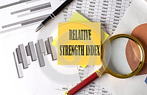 Relative Strength Index text on a sticky on the graph background with pen and magnifier