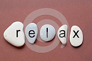 Relax as a word on flat stones in natural color and shape. A letter in black color on each stone isolated against a brown backgrou