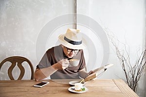 Relax Asian man drink coffee and read book in a modern style coffee shop