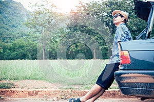 Relax asian man sitting inside car trunk with green nature background