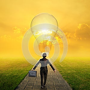 Relax business woman holding bag on Concrete road to Big idea bulb in Grass fields and sunset