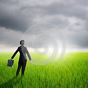 Relax business woman holding bag in green rice field and rainclouds