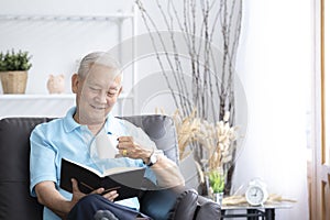 Relax elderly man sitting on sofa and reading interesting book in living room