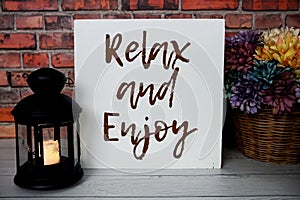 Relax and Enjoy text message with black lantern and daisy flowers bouquet on wooden background photo