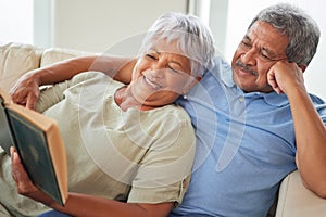 Relax, happy and senior couple reading a book together at home while relaxing and smiling on a couch. Mature or old