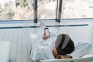 Relax in the hotel with a phone in hand. A man lying on a lounger by the pool and enjoying smartphone and great city