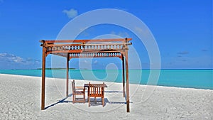 Relax on the Maldives beach. There is a canopy on the white sand, with a wooden table and chairs underneath.