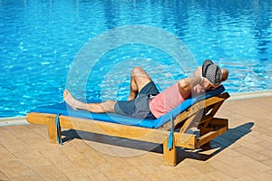 Relax in the pool summer. Young and successful man in hat lying on a sun lounger at the hotel on the background of sunset, concept