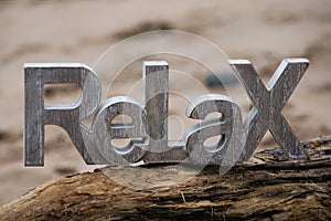 Relax Sign sitting on driftwood with beach behind