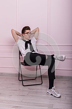 Relax stylish young hipster man in trendy glasses in a vintage white t-shirt in black jeans in fashionable leather sneakers is