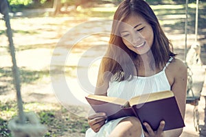 Relax woman holgind bible book read outdoors sitting on green garden in park. Young woman relaxation reading open book in autumn