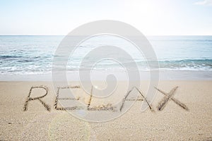 Relax word handwritten in sand on sunny beach