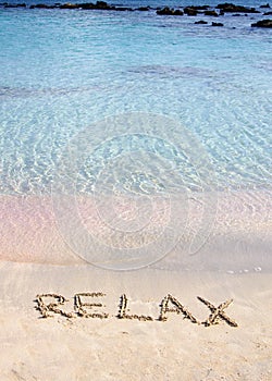 Relax word written in the sand, on a beautiful beach with clear blue waves in background