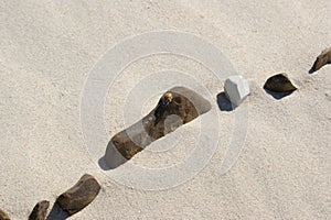 Relaxation on the beach. A row of stones in the light sand of the beach.