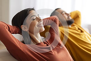 Relaxation Concept. Happy relaxed young couple leaning back on sofa at home