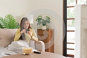 Relaxation concept, Young woman drinking coffee and watching television while lying on the couch