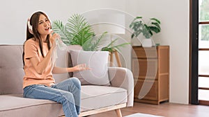Relaxation concept, Young woman in headphone sitting on the couch and hold water bottle to singing