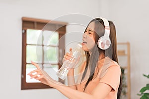 Relaxation concept, Young woman wear headphone listening music and hold water bottle to singing