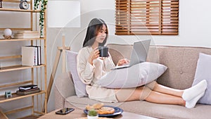Relaxation lifestyle concept, Young Asian woman surfing social media on laptop and drinking coffee