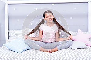 Relaxation and meditation. Girl child sit on bed in her bedroom. Kid prepare to go to bed. Pleasant time for evening