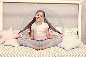 Relaxation and meditation. Girl child sit on bed in her bedroom. Kid prepare to go to bed. Pleasant time for evening