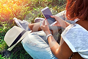 Relaxation with a mobile. Break time. Young woman using cellphone and sitting on the grass.