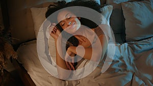 Relaxed African American curly-haired young woman sleepy beautiful girl lying in comfortable cozy bed night bedroom