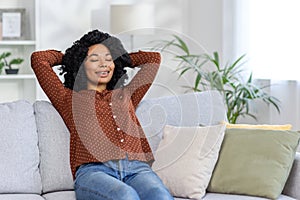 Relaxed african american woman enjoying a peaceful moment on a cozy couch at home with eyes closed
