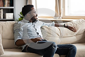 Relaxed african guy chill on sofa at home holding phone