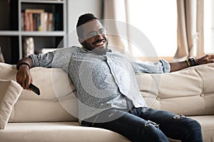 Relaxed african man hold remote control watching tv at home