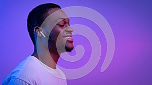 Relaxed African Man Listening Music In Wireless Airpods Earphones In Neon Light