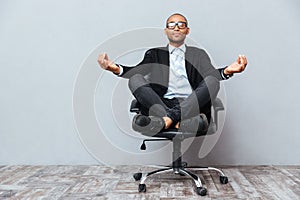 Relaxed african young man sitting and meditating on office chair