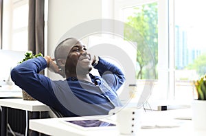 Relaxed Afro American business man sitting at his desk looking into the air.