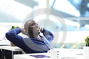 Relaxed afro american business man sitting at his desk looking into the air