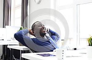 Relaxed Afro American business man sitting at his desk looking into the air.